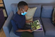 Mujer afroamericana con máscara facial leyendo documentos en la oficina moderna. distanciamiento social bloqueo de cuarentena durante la pandemia de coronavirus - foto de stock