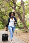 Donna afroamericana che indossa maschera in strada passeggiando per il parco, bevendo caffe '. in giro per la città durante covid 19 coronavirus pandemia. — Foto stock