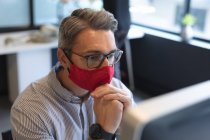 Homem caucasiano usando máscara facial olhando para a tela do computador no escritório. bloqueio de quarentena por distanciamento social durante a pandemia do coronavírus. — Fotografia de Stock