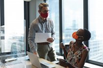 Diverse male and female colleagues wearing face masks talking to each other at modern office. social distancing quarantine lockdown during coronavirus pandemic — Stock Photo