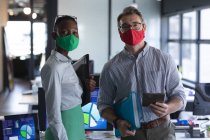 Portrait of diverse male and female colleagues wearing face masks at modern office. social distancing quarantine lockdown during coronavirus pandemic — Stock Photo