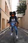Africano americano mulher vestindo máscara facial na rua andar de bicicleta para fora e sobre na cidade durante covid 19 coronavirus pandemia. — Fotografia de Stock