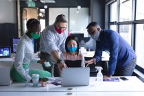 Diverse Kollegen tragen Gesichtsmasken per Laptop, während sie im modernen Büro zusammenarbeiten. Hygiene und soziale Distanzierung am Arbeitsplatz während der Coronavirus-Pandemie 19. — Stockfoto