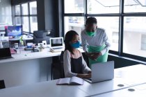 Diverse Kolleginnen tragen Gesichtsmasken mit Laptop im modernen Büro. Soziale Distanzierung von Quarantäne während der Coronavirus-Pandemie — Stockfoto