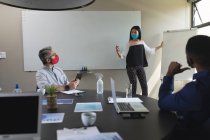 Азійка, одягнена в маску, дає презентацію різним колегам у залі зустрічей в сучасному офісі. Відстань до карантину під час пандемії коронавірусу — стокове фото