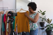 Vlogger afroamericana grabando un video en el armario. mostrando ropa a la cámara. auto aislamiento tecnología comunicación en el hogar durante coronavirus covid 19 pandemia. - foto de stock