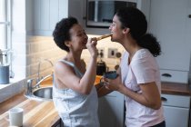 Happy mixed race lesbian couple having toast and coffee for breakfast in kitchen. self isolation quality time at home together during coronavirus covid 19 pandemic. — Stock Photo