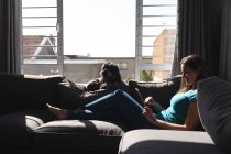 Улыбающаяся кавказка лежит на диване в гостиной с помощью планшета. наслаждаясь временем дома во время коронавирусного ковида 19 пандемического блокирования. — стоковое фото