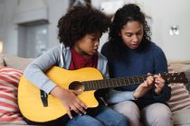 Змішана раса жінка і дочка сидять на дивані. грати на гітарі. самоізоляція якість сімейного часу вдома разом під час пандемії коронавірусу 19 . — стокове фото