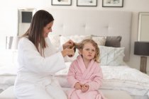 Белая женщина и дочь веселятся в спальне. Мама расчесывает дочке волосы. наслаждаясь временем дома во время коронавирусного ковида 19 пандемического блокирования. — стоковое фото
