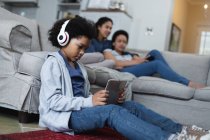 Ragazza mista seduta sul divano ad ascoltare musica usando tablet digitale. auto isolamento qualità famiglia tempo a casa insieme durante coronavirus covid 19 pandemia. — Foto stock