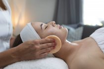 Mulher caucasiana deitada enquanto esteticista lhe dá um facial. cliente desfrutando de tratamento em um salão de beleza. — Fotografia de Stock