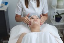 Donna caucasica sdraiata mentre estetista le dà un viso. cliente che si gode il trattamento in un salone di bellezza. — Foto stock