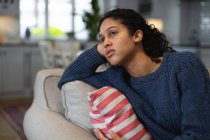 Mixed race woman sitting on couch looking sad. self isolation quality family time at home together during coronavirus covid 19 pandemic. — Stock Photo