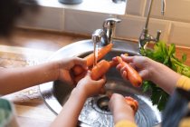 Couple préparant la nourriture laver les carottes dans l'évier de cuisine. auto isolement qualité famille temps à la maison ensemble pendant coronavirus covid 19 pandémie. — Photo de stock