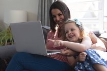 Caucasian mother and daughter having fun lying on couch using a laptop. enjoying quality time at home during coronavirus covid 19 pandemic lockdown. — Stock Photo