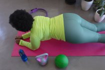 Mulher afro-americana deitada no tapete de exercícios a fazer exercício. auto isolamento aptidão em casa durante coronavírus covid 19 pandemia. — Fotografia de Stock