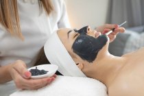 Mujer caucásica recostada mientras esteticista se aplica una mascarilla. cliente disfrutando del tratamiento en un salón de belleza. - foto de stock