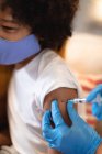 Fille de race mixte portant un masque facial étant vaccinée contre la grippe par un médecin féminin. auto-isolement à la maison pendant une pandémie de coronavirus covid 19 — Photo de stock