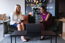 Diverses femmes d'affaires prenant un café à l'aide d'un ordinateur portable lors d'un appel vidéo dans un bureau créatif. technologie bureau moderne travail d'équipe remue-méninges. — Photo de stock