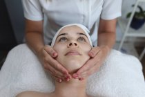 Mulher caucasiana deitada enquanto esteticista lhe dá um facial. cliente desfrutando de tratamento em um salão de beleza. — Fotografia de Stock