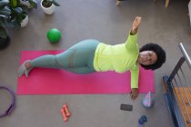 Vista ad alto angolo della donna afro-americana sdraiata sul tappeto esercizio di lavoro fuori. auto isolamento fitness a casa durante il coronavirus covid 19 pandemia. — Foto stock