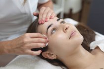 Kaukasische Frau lehnt sich zurück, während Kosmetikerin sich die Augenbrauen abwischt. Kundin genießt Behandlung im Schönheitssalon. — Stockfoto