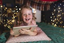 Menina caucasiana deitada no travesseiro e cobertor verde no quarto usando tablet e sorrindo. desfrutando de tempo de qualidade em casa durante coronavírus covid 19 bloqueio pandêmico. — Fotografia de Stock