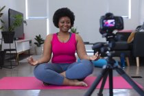 Vlogger afroamericana grabando un video. sobre la meditación. auto aislamiento tecnología comunicación en el hogar durante coronavirus covid 19 pandemia. - foto de stock