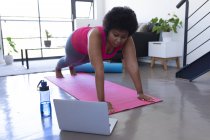 African american woman using laptop exercising wearing sports clothes. self isolation fitness technology communication at home during coronavirus covid 19 pandemic. — Stock Photo