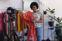 Vloggeuse afro-américaine enregistrant une vidéo en garde-robe. montrant des vêtements à la caméra. auto-isolement technologie communication à la maison pendant coronavirus covid 19 pandémie. — Photo de stock