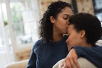 Lesbisches Paar mit gemischter Rasse küsst sich in der Küche auf die Stirn Selbstisolierung Qualität Zeit zu Hause zusammen während Coronavirus covid 19 Pandemie. — Stockfoto