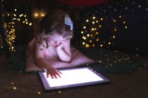 Кавказка лежит в спальне, используя цифровые планшеты в вечернее время. наслаждаясь временем дома во время коронавирусного ковида 19 пандемического блокирования. — стоковое фото