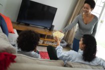 Casal lésbico misto e filha sentados no sofá assistindo TV e comendo pipocas. auto isolamento tempo familiar de qualidade em casa juntos durante coronavírus covid 19 pandemia. — Fotografia de Stock