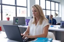Kaukasische Geschäftsfrau sitzt mit einem Laptop in einem modernen Büro. Business moderne Büroarbeitstechnologie. — Stockfoto