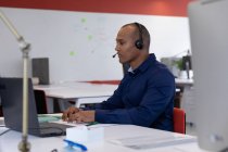Homem de negócios de raça mista sentado usando fones de ouvido usando laptop no escritório moderno. negócio moderno escritório tecnologia do local de trabalho. — Fotografia de Stock