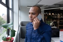 Uomo d'affari misto in piedi alla finestra utilizzando lo smartphone in un ufficio moderno. affari ufficio moderno tecnologia sul posto di lavoro. — Foto stock