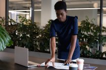 Gemischte Geschäftsfrau, die mit Laptop im modernen Büro steht und Papierkram erledigt. Business moderne Büroarbeitstechnologie. — Stockfoto
