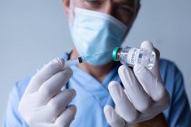 Medico maschio caucasico con maschera facciale in piedi e siringa di riempimento. igiene del personale sanitario durante la pandemia di coronavirus covid 19. — Foto stock