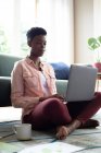 Afro-americana sentada no chão usando laptop trabalhando em casa. ficar em casa em auto-isolamento durante o confinamento de quarentena. — Fotografia de Stock