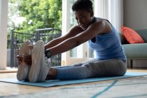 Mujer afroamericana realizando ejercicio de estiramiento en casa. permaneciendo en casa en aislamiento en cuarentena - foto de stock