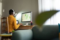 Mujer afroamericana que usa auriculares con computadora mientras trabaja desde casa. permaneciendo en casa en aislamiento en cuarentena - foto de stock