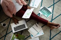 Африканська американка сидить на підлозі, використовуючи ноутбук, що проходить через папери з дому. Перебуваючи вдома в ізоляції під час карантину.. — стокове фото