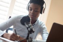 Mujer afroamericana usando auriculares usando micrófono y computadora portátil haciendo notas durante la videollamada. comunicación en línea, permanecer en casa en aislamiento durante el bloqueo de cuarentena. - foto de stock