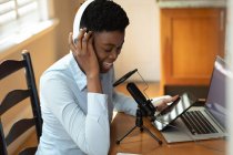 Mujer afroamericana usando auriculares usando micrófono y portátil. comunicación en línea, permanecer en casa en aislamiento durante el bloqueo de cuarentena. - foto de stock