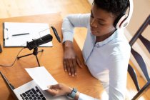 Afro-americana usando fones de ouvido usando microfone e laptop. comunicação on-line, ficar em casa em auto-isolamento durante o bloqueio de quarentena. — Fotografia de Stock