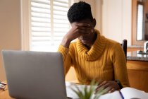 Mulher afro-americana usando laptop esfregando os olhos na cozinha. ficar em casa em auto-isolamento durante o confinamento de quarentena. — Fotografia de Stock