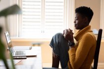 Africano mulher americana usando laptop e beber café na cozinha. ficar em casa em auto-isolamento durante o confinamento de quarentena. — Fotografia de Stock