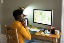 Mujer afroamericana hablando por teléfono inteligente y usando la computadora mientras trabaja desde casa. permaneciendo en casa en aislamiento en cuarentena - foto de stock