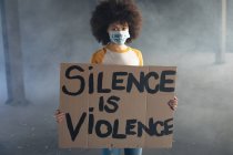 Mulher de raça mista usando máscara facial com slogan segurando sinal de protesto. gênero fluido lgbt identidade conceito de igualdade racial. — Fotografia de Stock